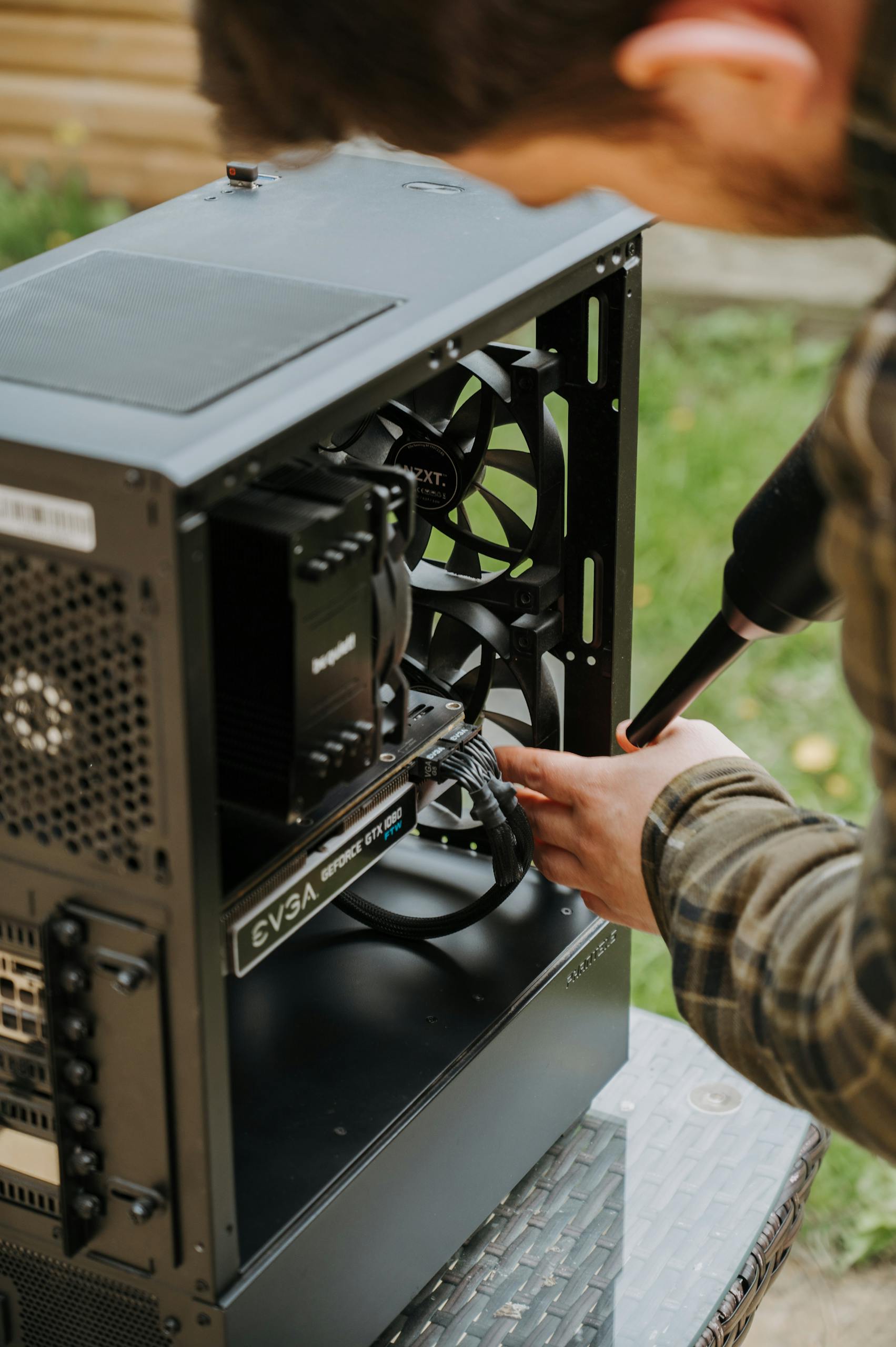 Person using an air duster to clean a desktop PC case outdoors for maintenance.